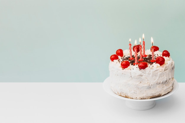 Foto verlichte kaarsen op verjaardagscake op caketribune tegen blauwe achtergrond