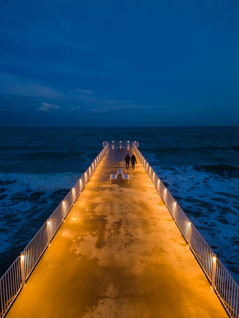 Verlichte pier met dramatische lucht boven stormachtige donkere zee 's avonds Varna Bulgarije