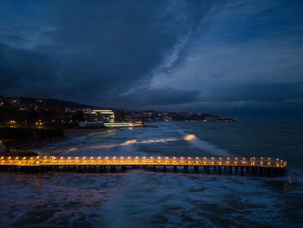 Verlichte pier met dramatische lucht boven stormachtige donkere zee 's avonds Varna Bulgarije