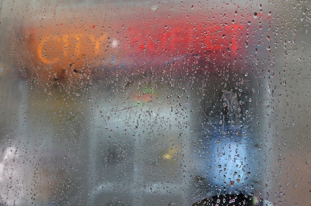 Verlichte tekst gezien door een nat glasvenster van een bus