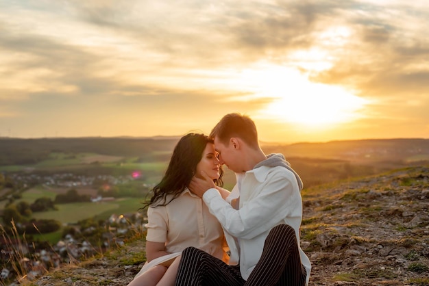 Verliefd stel, een jongen en een meisje zitten op een berg bij zonsondergang zoenen en knuffelen