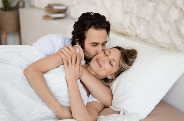 Verliefde blanke paar ontspannen in bed thuis genieten van saamhorigheid en tederheid verliefd man vrouw kussen