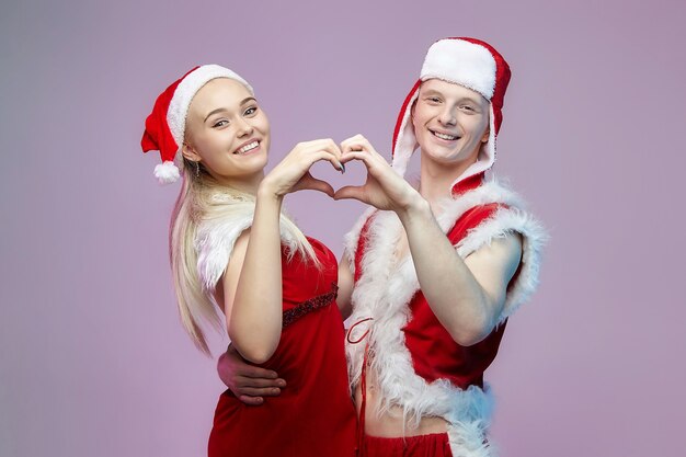 Verliefde jongen en meisje in kerstkostuums vouwden hun handen in de vorm van een hart. Kerstmis en Nieuwjaar concept