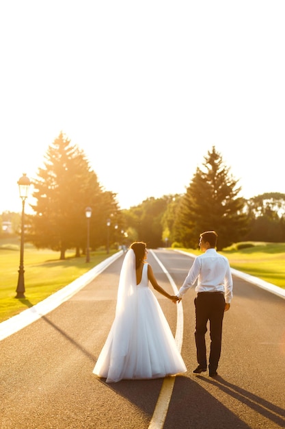 Verliefde paar gaan hand in hand op weg om de zonsondergang te ontmoeten Bruid en bruidegom lopen op de weg