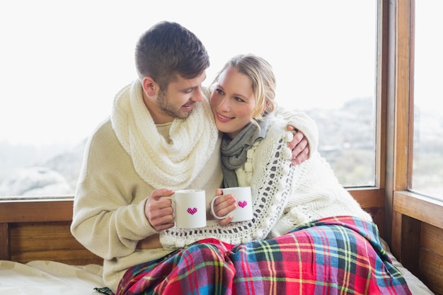 Verliefde paar in de winter dragen met cups tegen raam