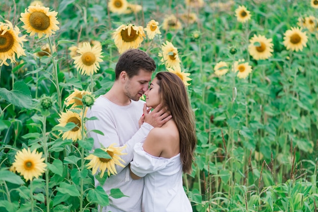 Verliefde paar in witte jurken kussen, glimlachen, hughing in een veld met zonnebloemen