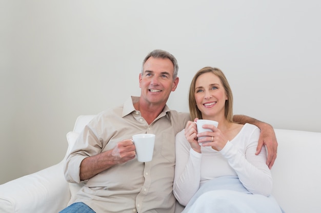 Verliefde paar met koffie cups wegkijken in de woonkamer