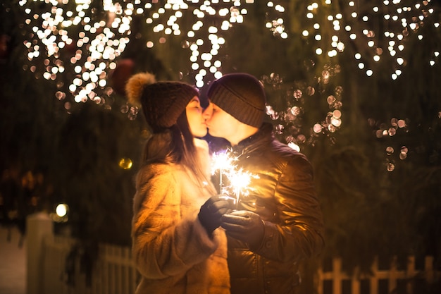 Verliefde paar met sprankelend Bengaals licht zoenen in de buurt van een kerstboom