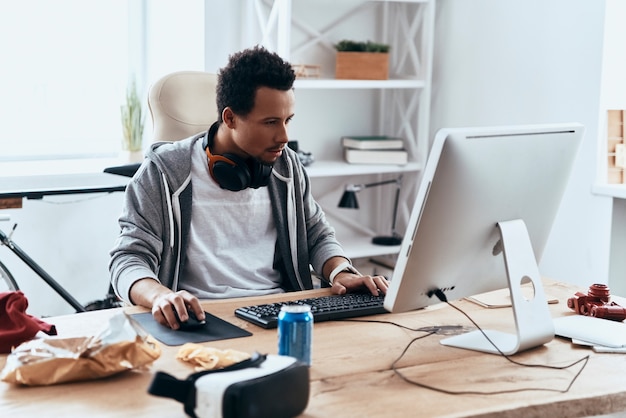 Verloren in de virtuele realiteit. Geconcentreerde jongeman in vrijetijdskleding die computer gebruikt terwijl hij thuis tijd doorbrengt