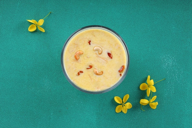 Vermecelli Payasam или Kheer, основное сладкое блюдо Южной Индии, приготовленное с использованием вермишели, молока, сахара и сухих орехов и украшенное цветком золотого дождя на окрашенном зеленом фоне, выборочный фокус.
