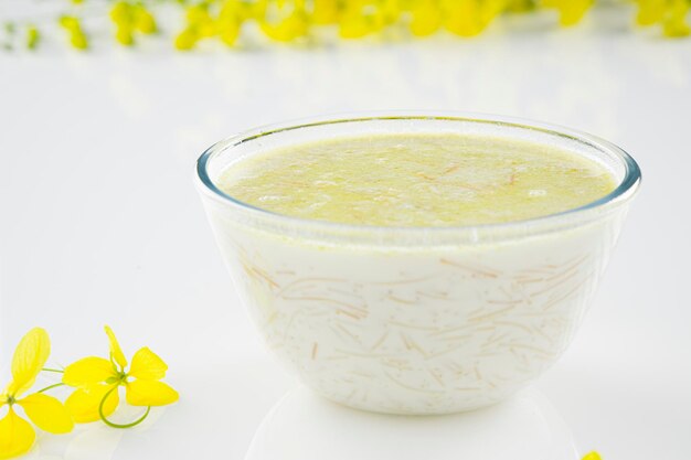 베르메첼리 파야삼(Vermecelli Payasam) 또는 키어(Kheer), 버미첼리, 우유, 설탕, 마른 견과류를 사용하여 만든 남부 인도의 달콤한 요리는 흰색 배경에 황금빛 샤워 꽃으로 배열되어 선택적인 초점을 맞춥니다.