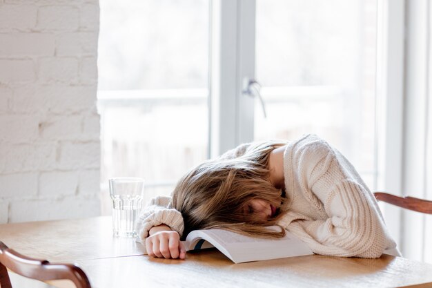 Vermoeid meisje in witte sweater met boek bij keuken