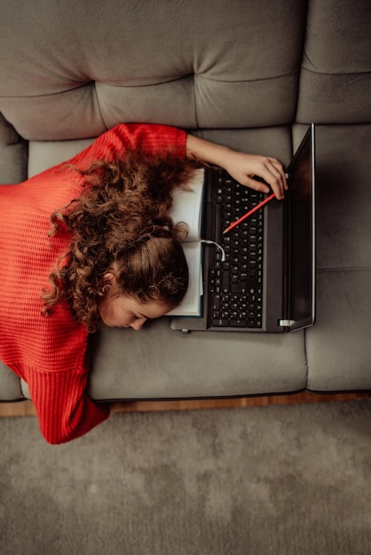 Vermoeid meisje slaapt naast een laptopVermoeid meisje van thuisonderwijs op afstandOnline onderwijs voor kinderen tijdens quarantaine