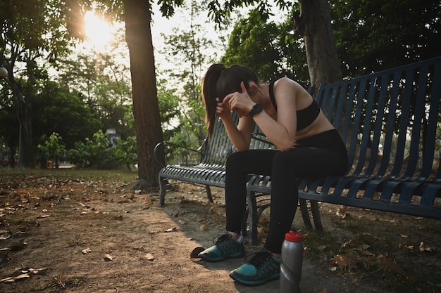 Foto vermoeide atletische vrouw die een pauze neemt van fitnesstraining zittend op een bankje in het park met prachtig zonlicht