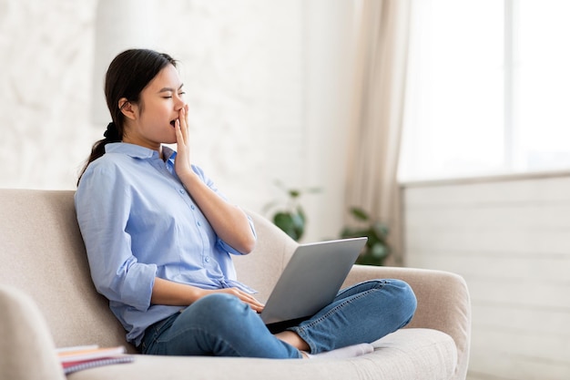 Vermoeide Aziatische dame freelancer die vanuit huis werkt met behulp van laptop