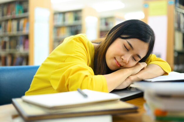 Vermoeide aziatische studente die een dutje doet in de universiteitsbibliotheek tijdens de voorbereiding op examens