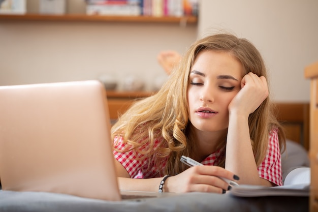 Vermoeide blonde student slaapt tijdens saaie online les thuis vanwege de wereldwijde covid-19 pandemie.