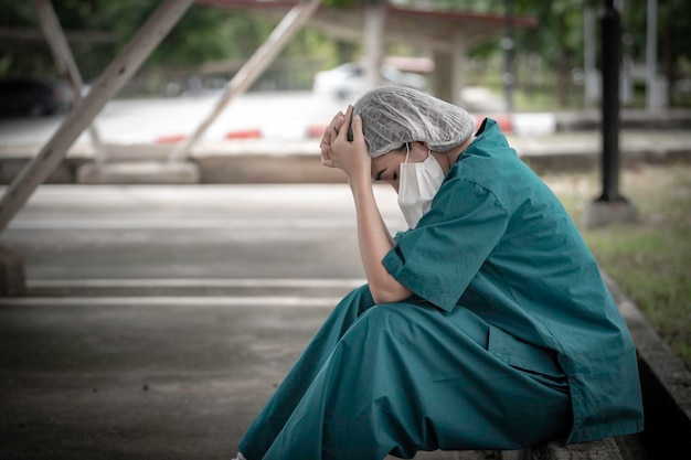Vermoeide depressieve vrouwelijke Aziatische scrubverpleegster draagt gezichtsmasker blauw uniform zit op ziekenhuisvloer Jonge vrouwelijke arts gestrest door hard werken