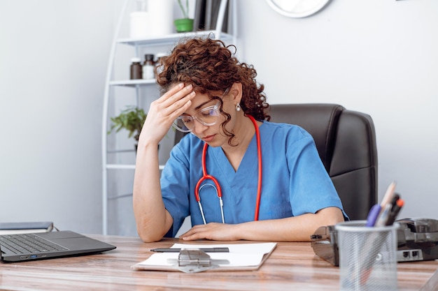 Foto vermoeide depressieve vrouwelijke dokter die alleen in het kantoor zit.