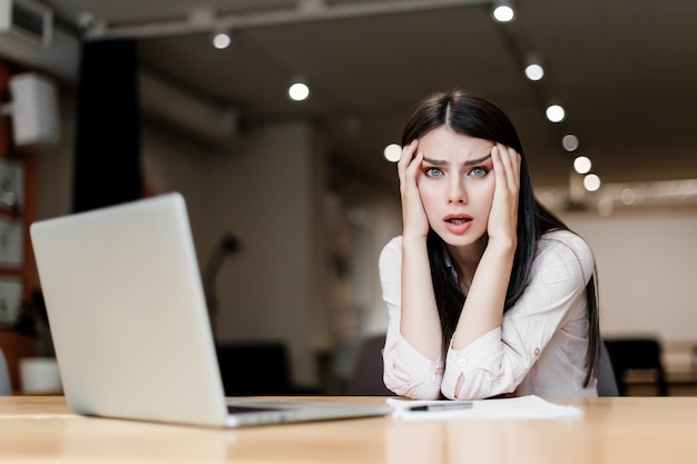 Vermoeide en uitgeputte verwarde vrouw met laptop op het kantoor