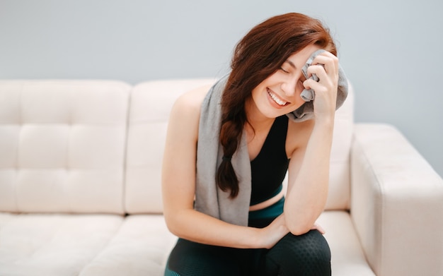 Vermoeide gelukkige fitte vrouw met een handdoek op haar gezicht na een thuis workoutconcept van fitness en gezondheid