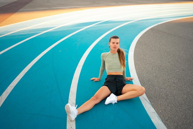 Foto vermoeide, gelukkige vrouwelijke hardloper die na het hardlopen rust, zit op de loopbaan.