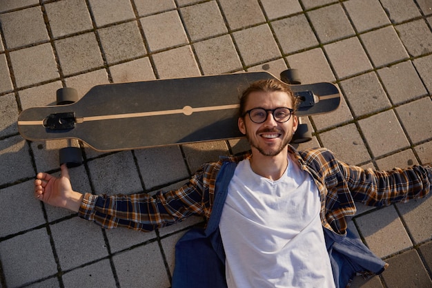 Foto vermoeide hipster die na de training op een skateboard ligt en zich ontspant bij zonsondergang.