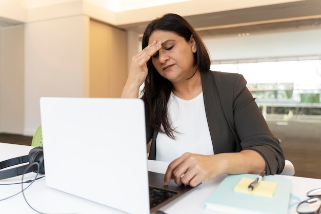 Vermoeide Indiase zakenvrouw die hoofdpijn heeft met behulp van een laptopwerkproject op kantoor