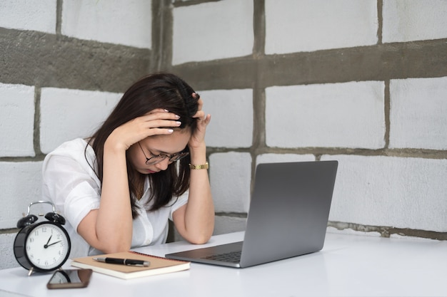 Vermoeide jonge Aziatische vrouw in glazen die met laptop in bureau werken.