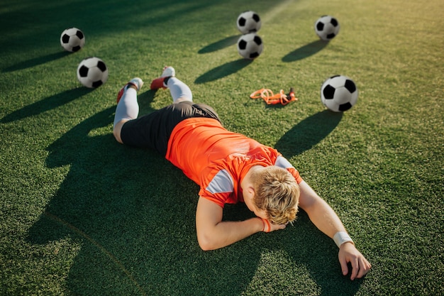 Vermoeide jonge speler die op gazon ligt met gezicht dat naar de grond wordt gedraaid