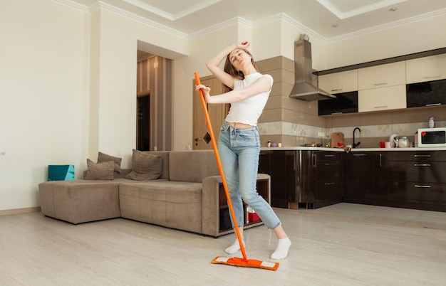 Vermoeide jonge vrouw van het schoonmaken van het appartement staat met een dweil Huis schoonmaak concept