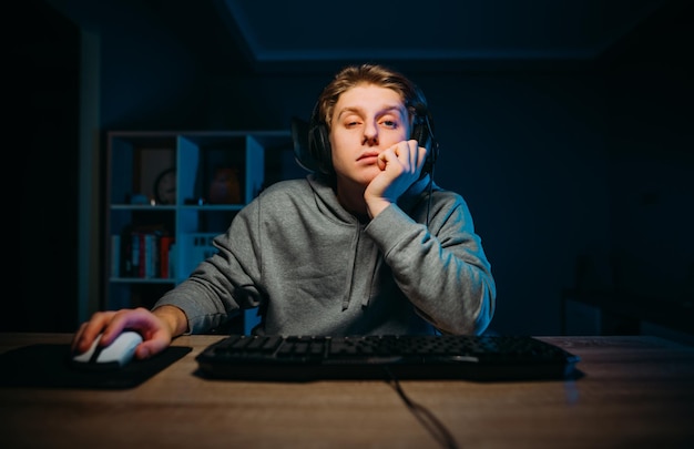 Vermoeide jongeman in headset die thuis videogames speelt op de computer in de kamer met blauw licht