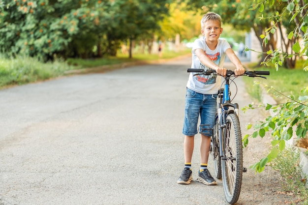 Vermoeide jongen in een t-shirt en denim korte broek leunt op zijn fiets na een lange fietsrit in het park