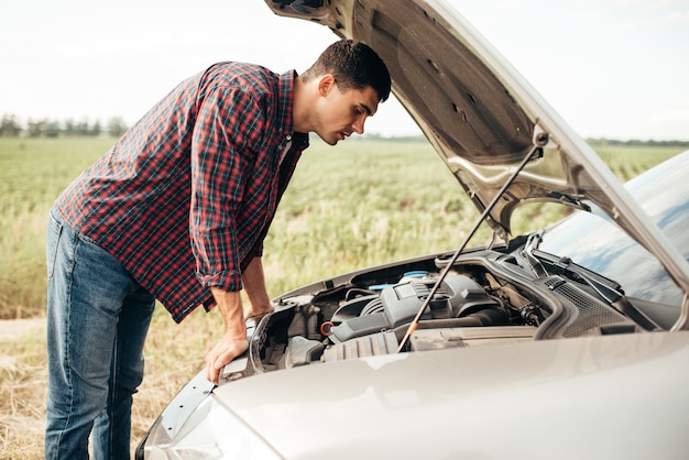 Vermoeide man probeert een kapotte auto te repareren