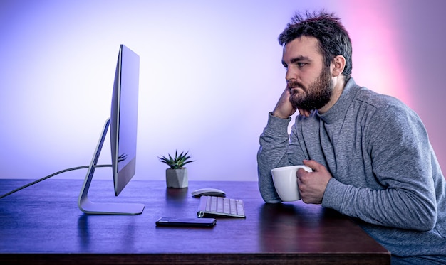 Vermoeide man zit voor een computer met een kopje koffie gekleurde verlichting