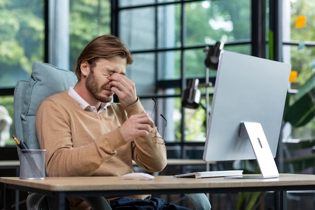 Vermoeide mannelijke freelancer-programmeur wrijft in zijn ogen lijdt aan oververmoeidheid, ongemak, lang zittend werk