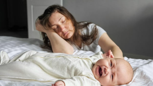 Vermoeide moeder slaapt zittend op de vloer in de buurt van huilende babymeisje