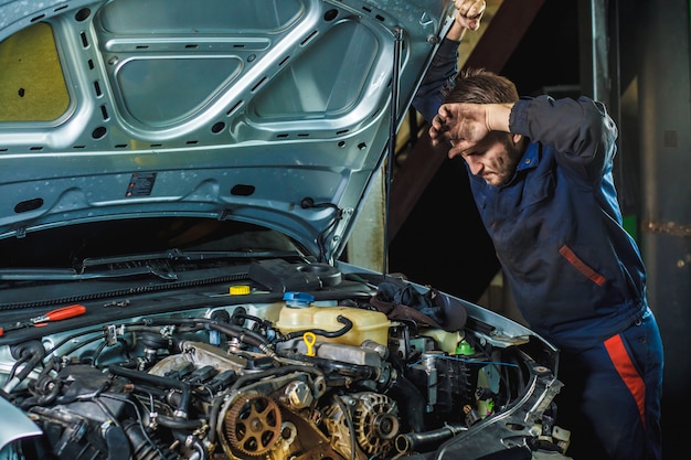 Vermoeide monteur kijkt naar de motor en veegt zijn voorhoofd af met zijn hand.