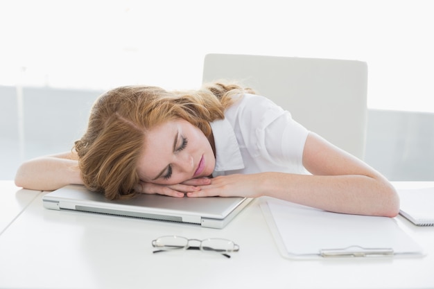 Vermoeide onderneemster met hoofd op laptop in bureau