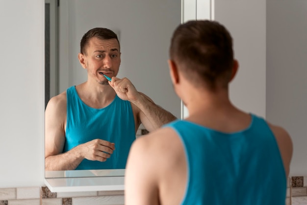 Vermoeide ongeschoren man poetst zijn tanden in de badkamer voor de spiegel Ochtendroutine Mondhygiëne