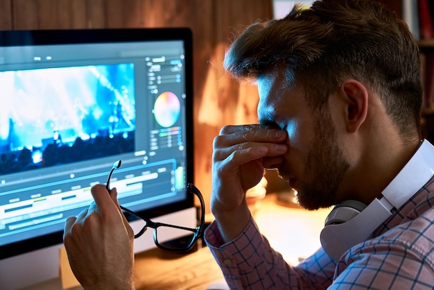 Foto vermoeide overwerkte jonge zakenman die zijn bril uittrekt en vermoeide droge ogen wrijft na lang werk op de computer laat in de donkere nacht met astigmatisme, gezichtsproblemen, slecht gezichtsvermogen, oogvermoeidheid, pijn.