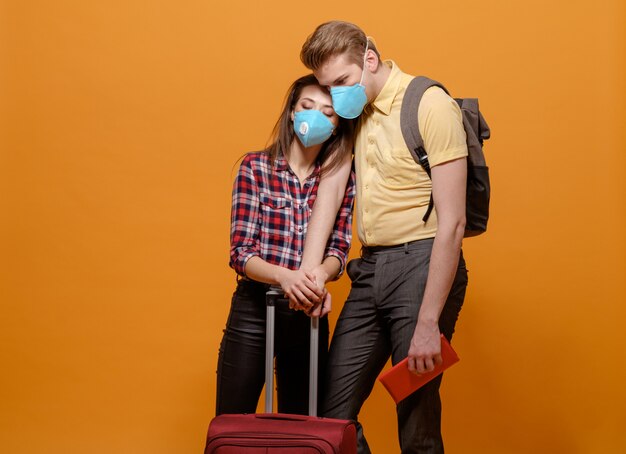 Vermoeide toeristen, reizigers man en vrouw in medische maskers op een geeloranje, coronavirus pandemie, gesloten grenslanden, grote koffer