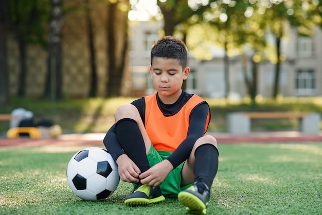 Vermoeide voetballer op openluchtstadion dat de schoenveter op zijn opleidingslaarzen koppelt