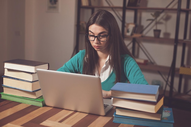 Vermoeide vrouw in glazen met veel boeken en laptop werkt aan de houten tafel