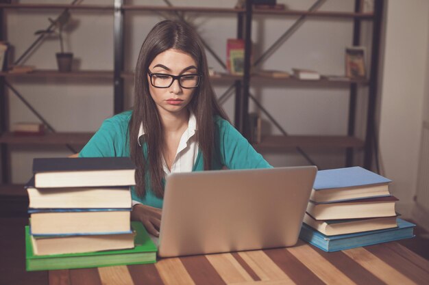 Vermoeide vrouw in glazen met veel boeken en laptop werkt aan tafel