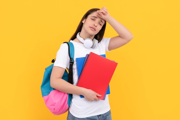 Vermoeide vrouw met koptelefoon houdt notitieboekje op gele achtergrond terug naar school