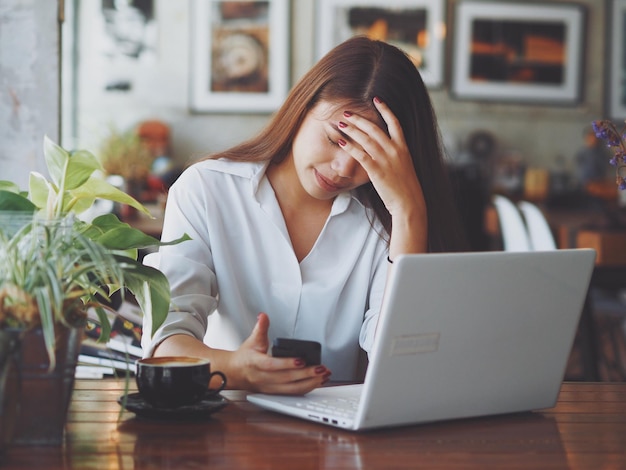 Vermoeide vrouw met mobiele telefoon en laptop.