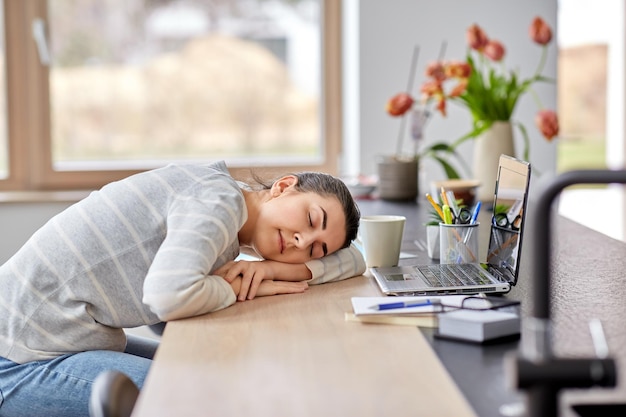 vermoeide vrouw slaapt op tafel met laptop thuis
