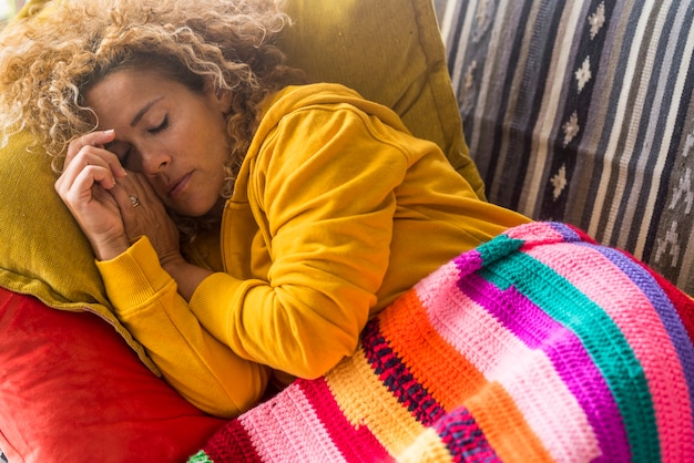 Vermoeide vrouw slaapt overdag op de bank met kleurrijke hoes - stress en het binnenleven op zondag - mooie vrouwelijke mensen die alleen op de bank slapen