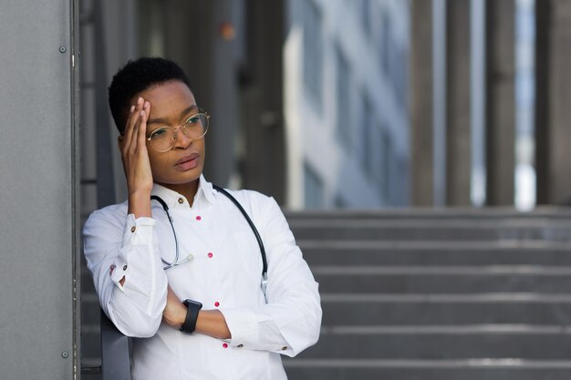 Vermoeide vrouwelijke arts na een zware dag in de kliniek een Afro-Amerikaanse vrouw in de kliniek met ernstige hoofdpijn en depressie na overwerk